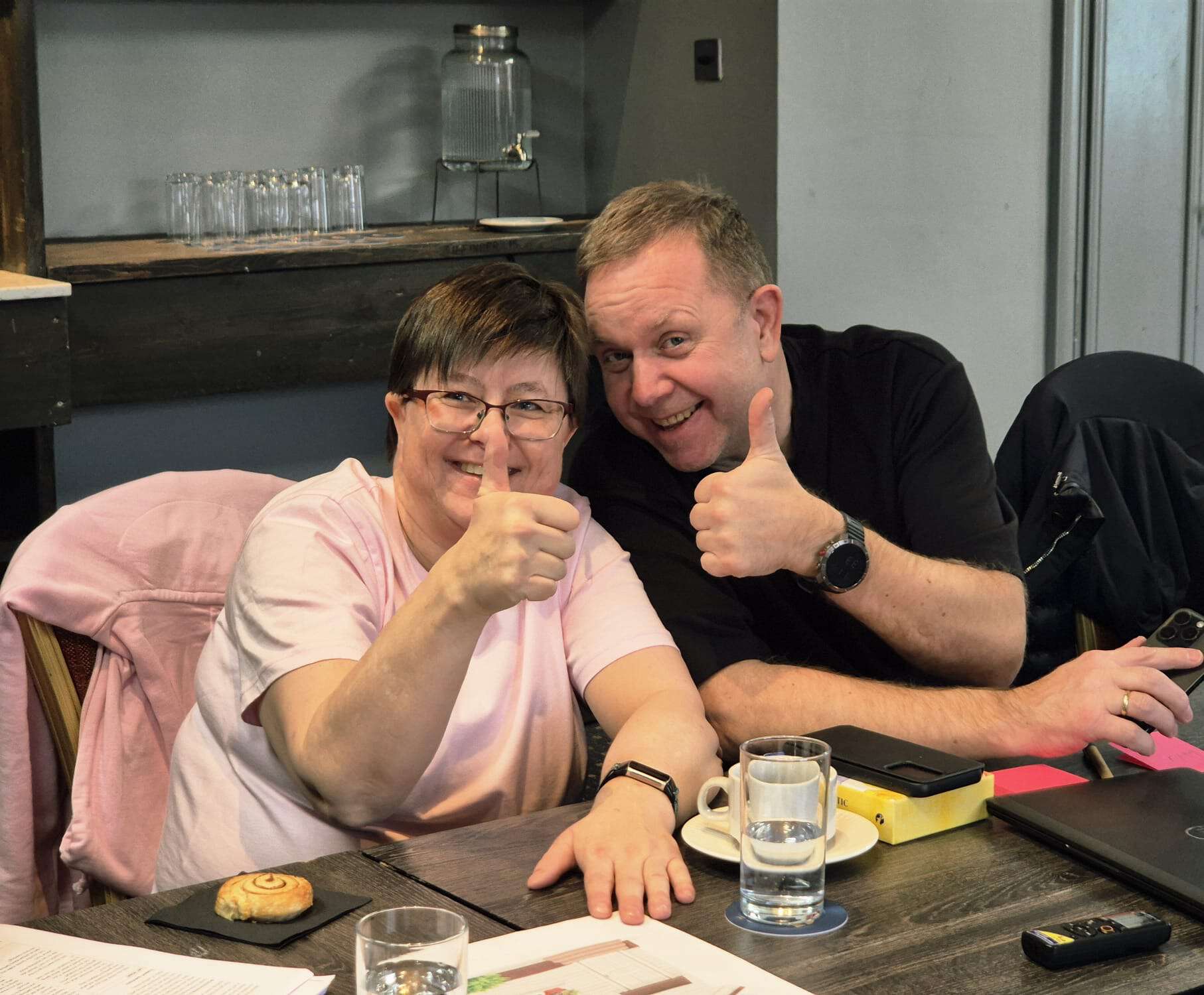 en kvinne og mann sittende ved et bord, begge viser tommel opp