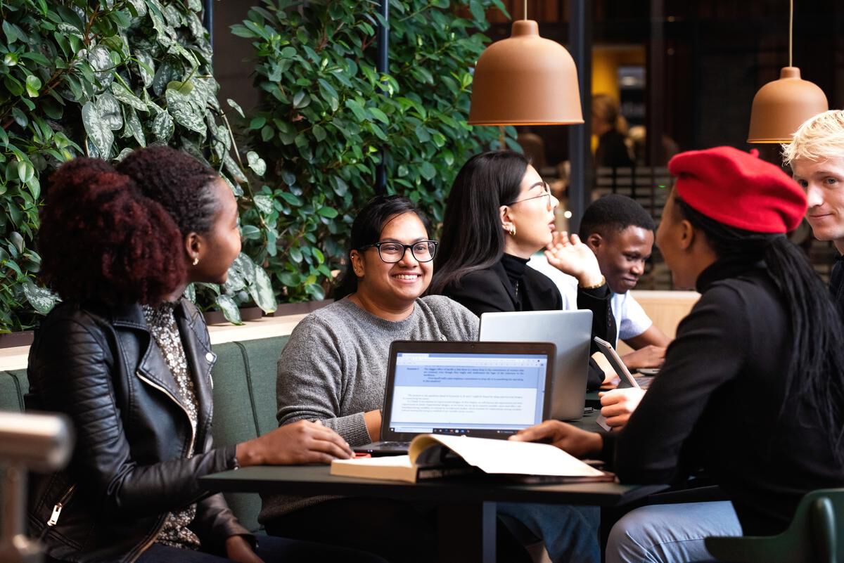 The picture shows students talking together at a table on campus.