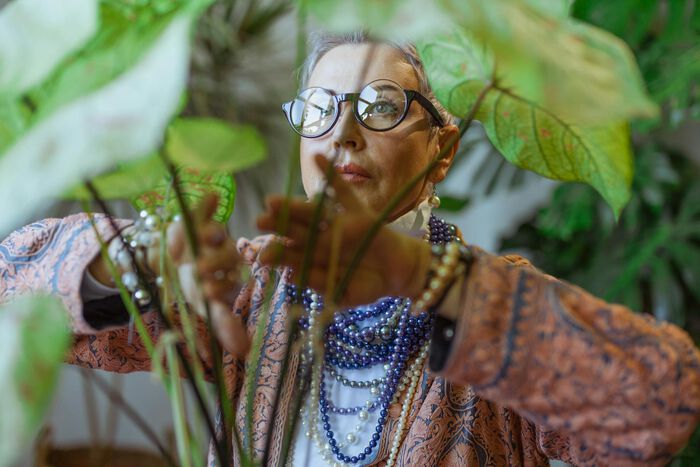 Bildet viser en eldre kvinne som står bak en plante.