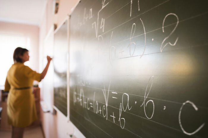 Bildet viser lærer som skriver tall og matematiske formler på tavlen.