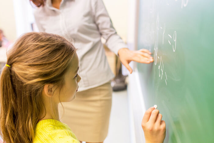 Photo showing teacher helping a pupil do a math equation on the blackboard