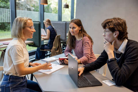 Tre studenter snakker sammen rundt en pult