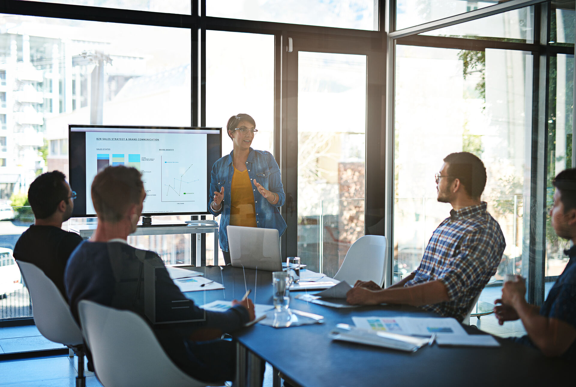 5 people having a meeting at a sun-filled office with wide window
