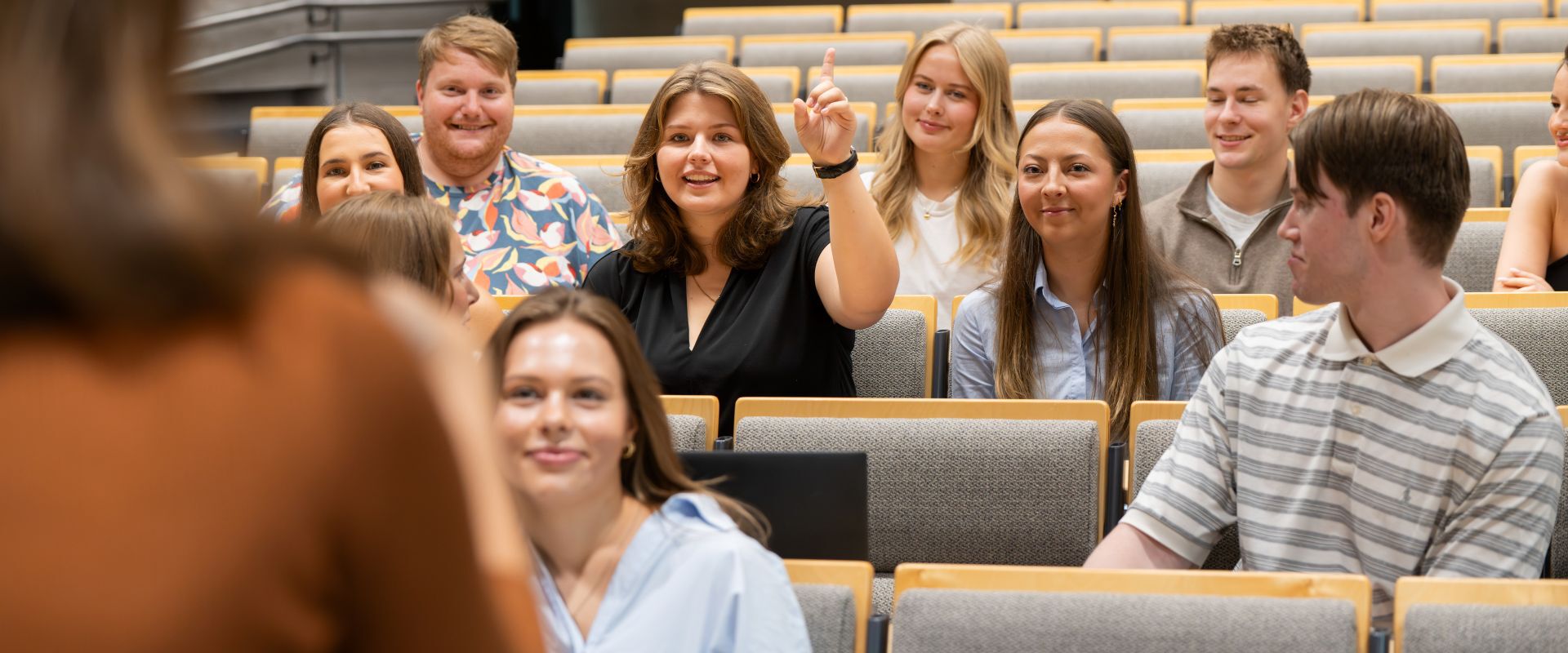 Smilende student i fokus, mann, flere studenter rundt, auditorium