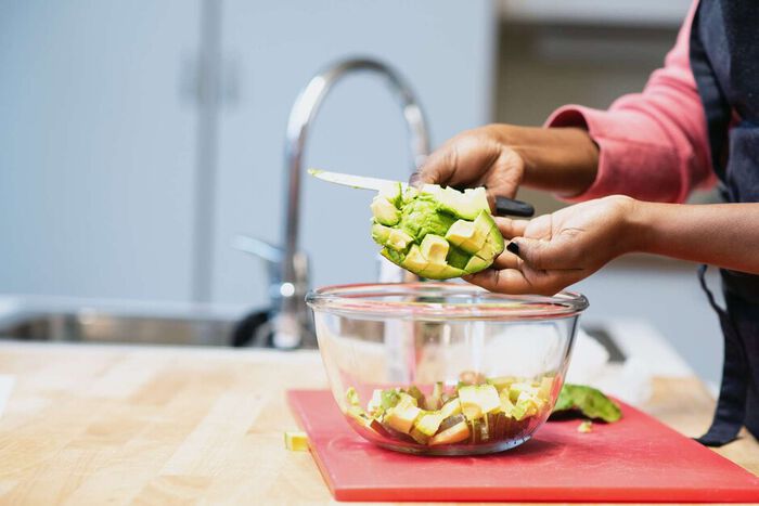 Oppkuttet avocado, glassbolle, kniv, hender, rød skjærefjøl