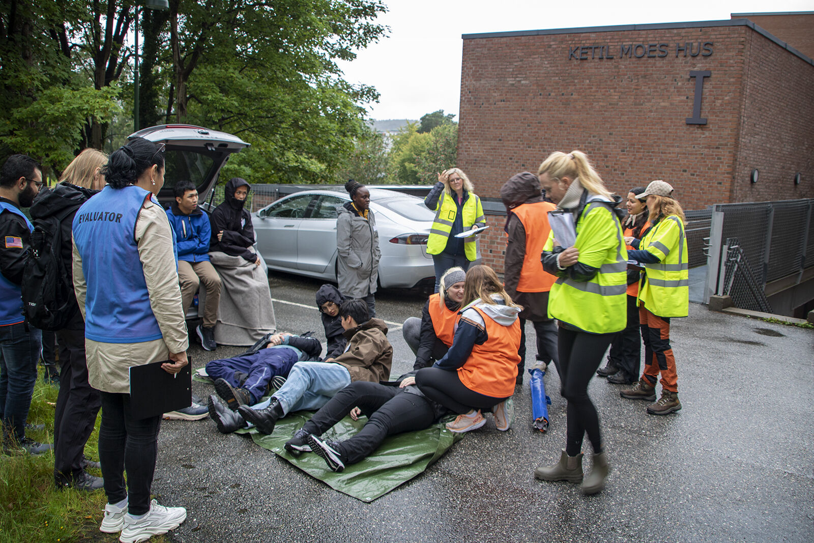 Bildet viser studenter som spiller rollen som skadet og som hjelpepersonell. De skadde har blitt flyttet til en bil i nærheten, og ligger på bakken.