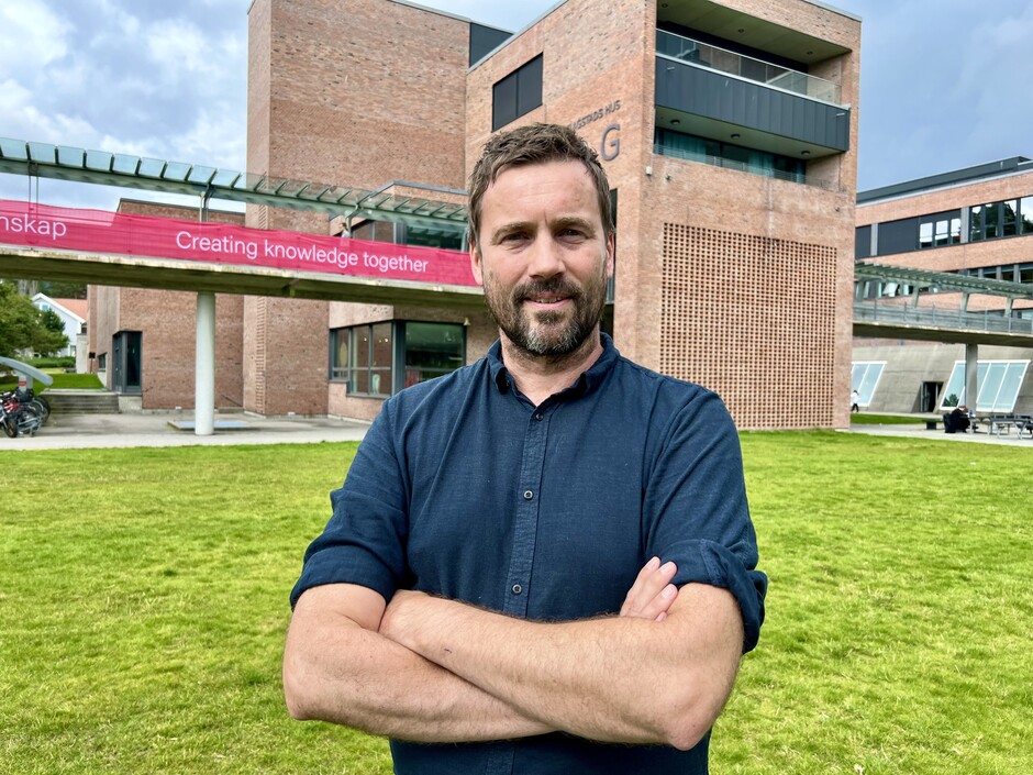 Close-up of professor Daniel Nordgård standing on the campus-lawn with his arms crossed.
