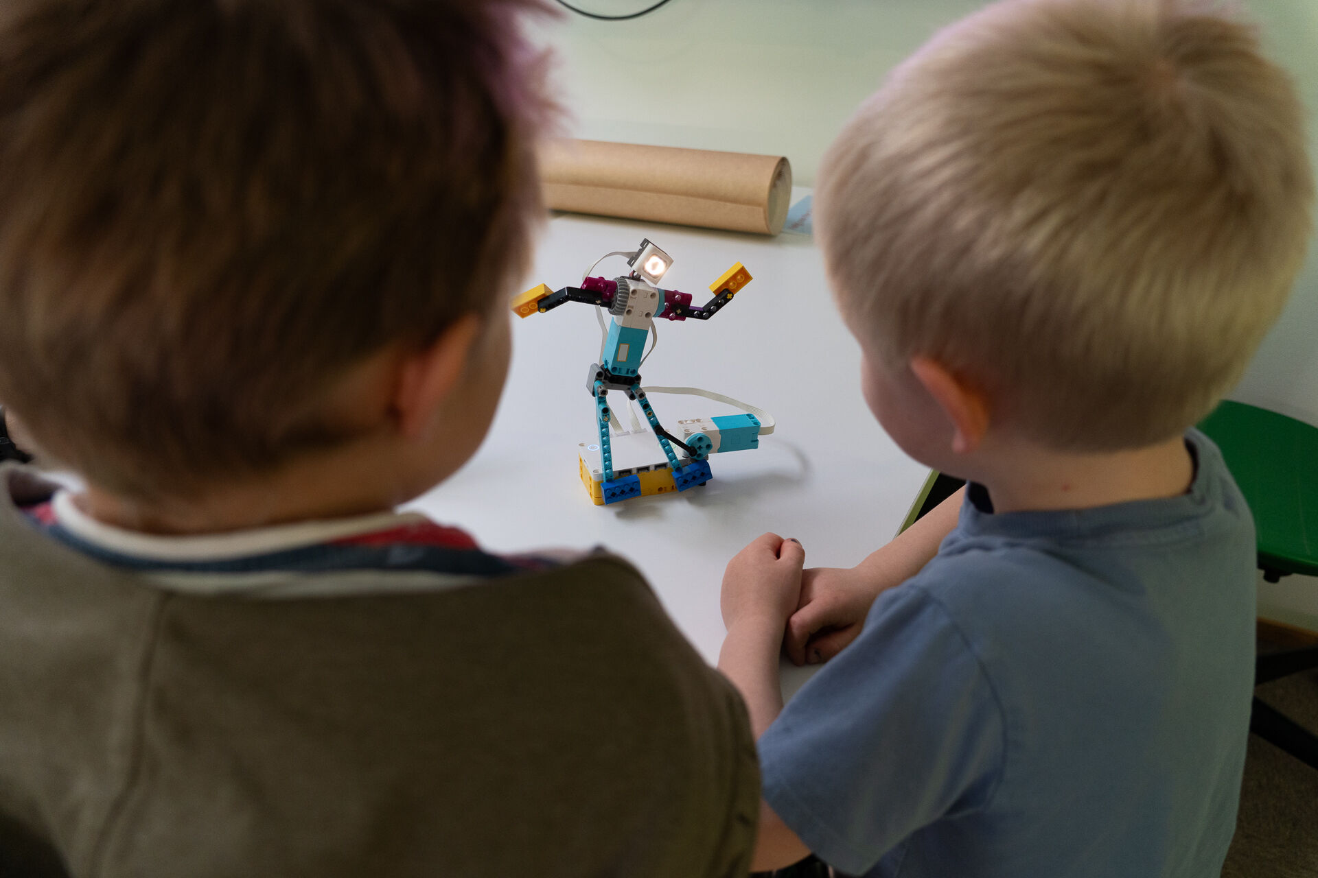 Biletet viser to barn som ser på ein robot av lego