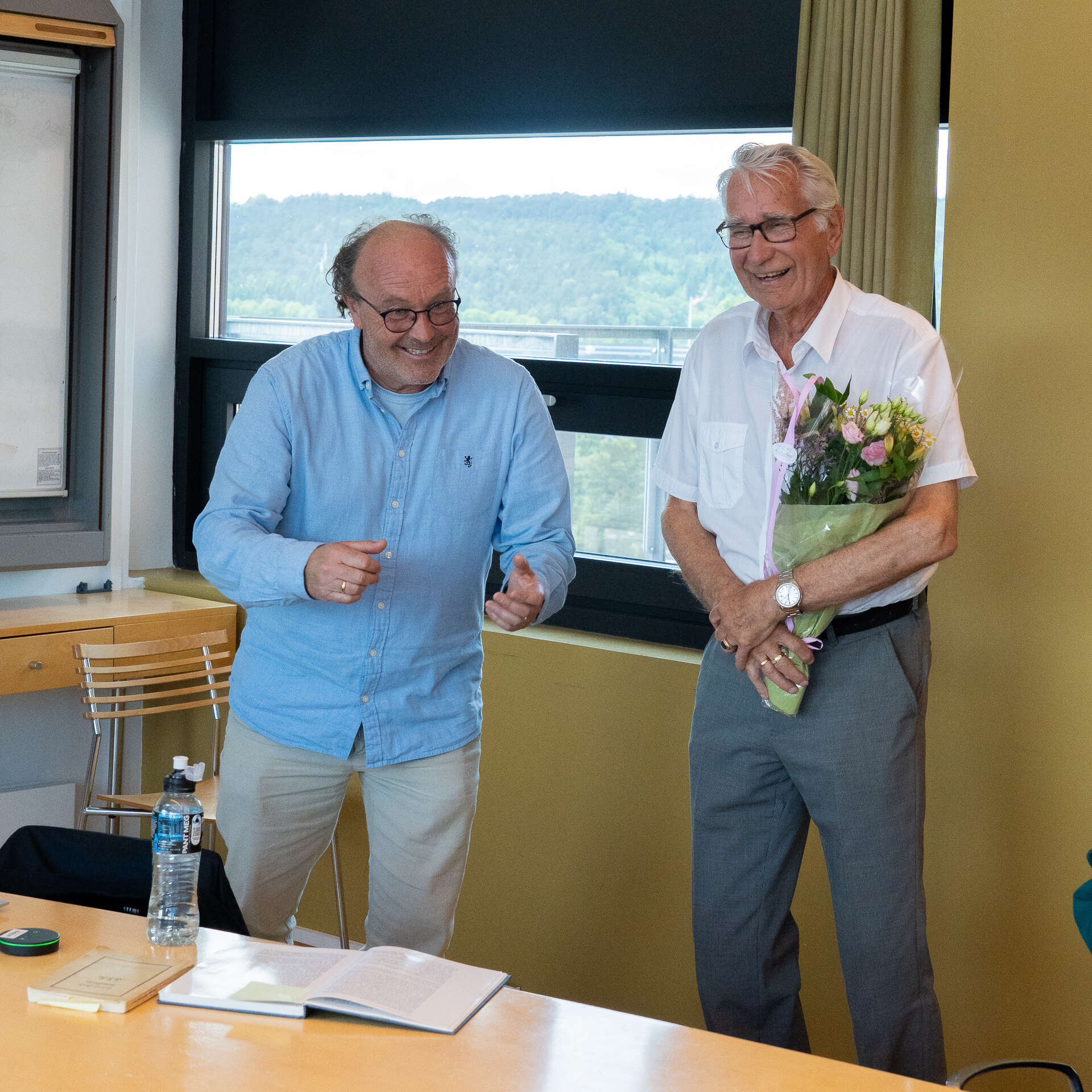Bildet viser to menn, smiler, en holder en blomsterbukett
