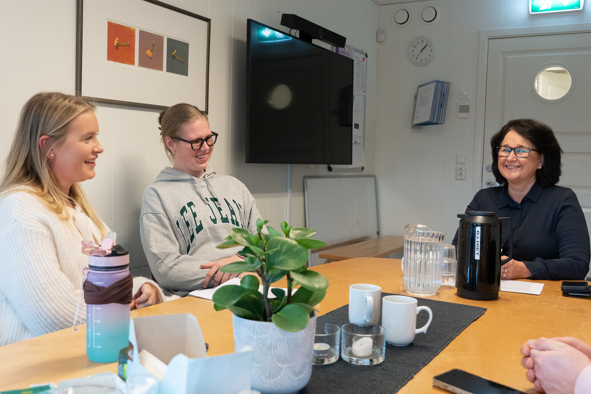 Ingrid, Helene, Jorunn rundt møtebord. Plante, kopper, telys.