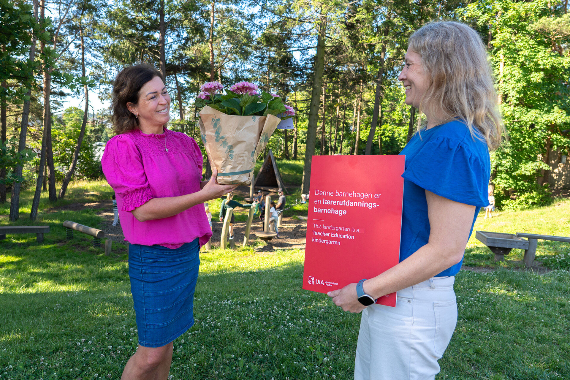 Bildet viser overrekkelse av blomst og skilt med teksten denne barnehagen er en lærerutdanningsbarnehage, ute i barnehageområde