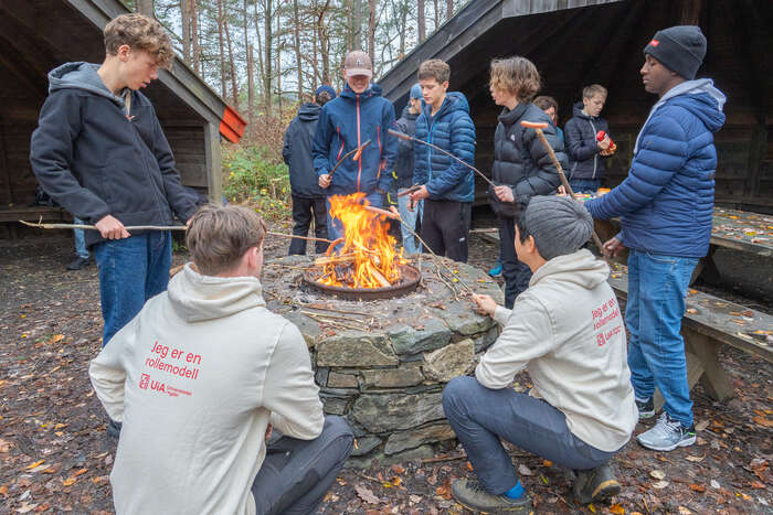 Bildet viser ei gruppe elevar rundt eit bål, to barnehagelærarar i front