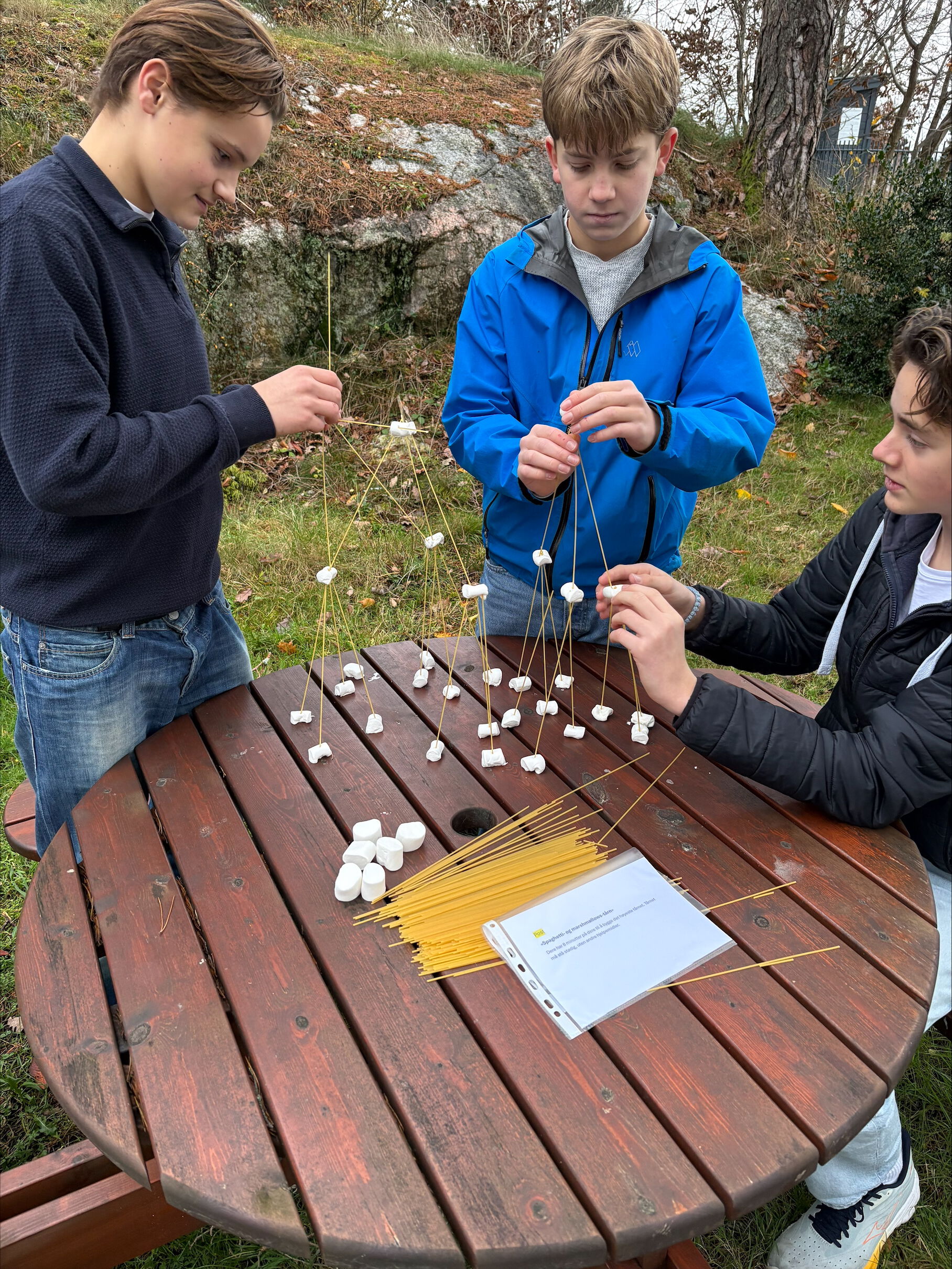 Bildet viser tre gutter som samarbeider om å bygge tårn av marshmellows og spaghetti