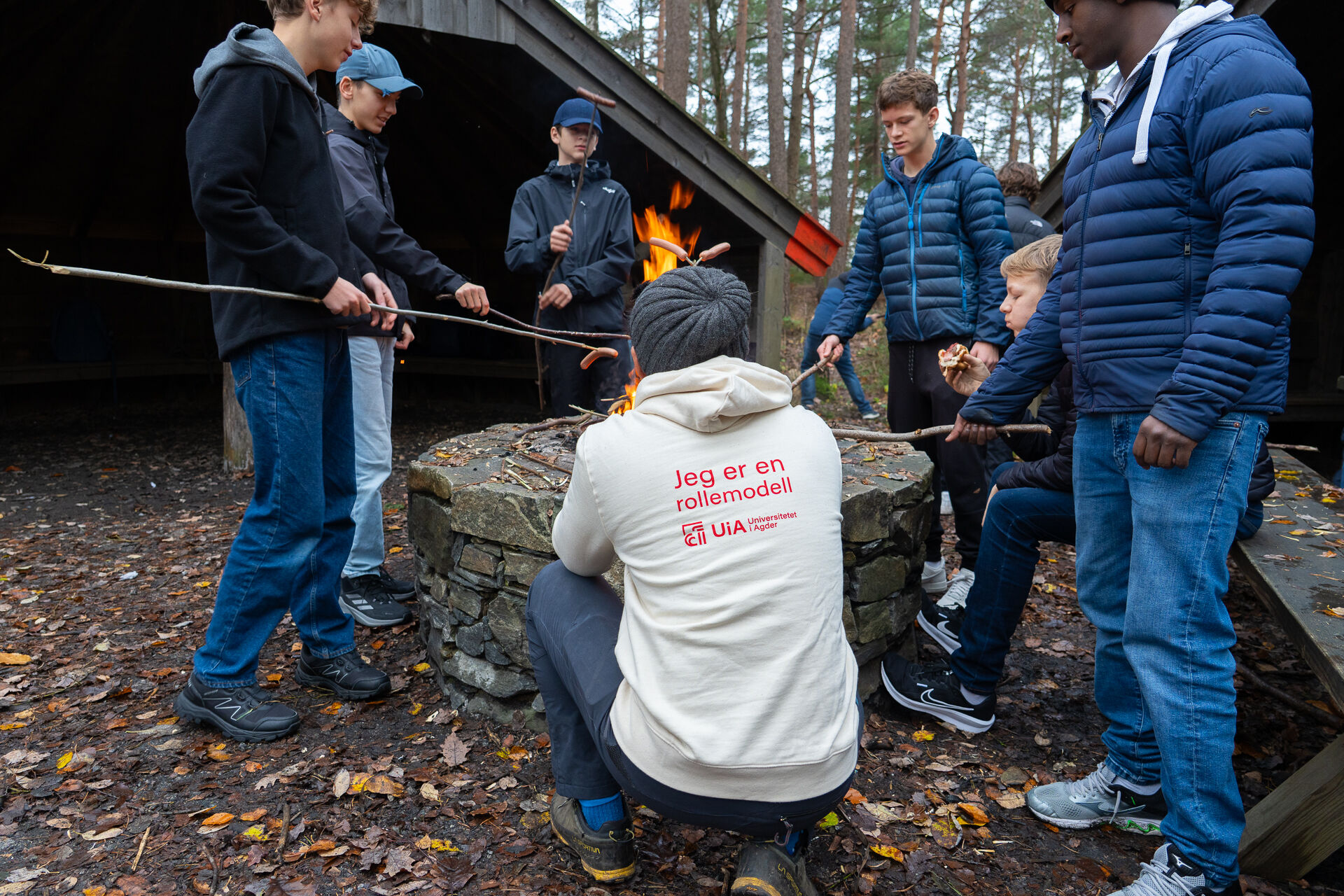 Bildet viser en gruppe som griller pølser på bål. En med ryggen til med påskriften Jeg er en rollemodell på genseren