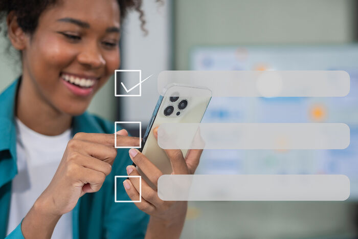 Bildet viser en dame i bakgrunnen med en mobil, over bildet er det lagt på illustrasjon av digitale valgbokser