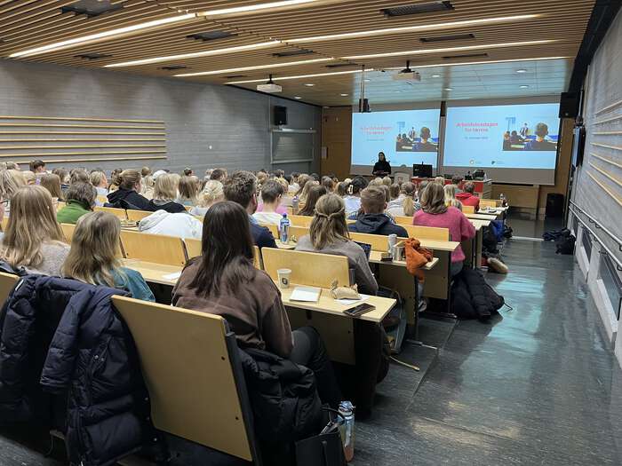 Bildet viser studenter i auditorium, presentasjon på tavle