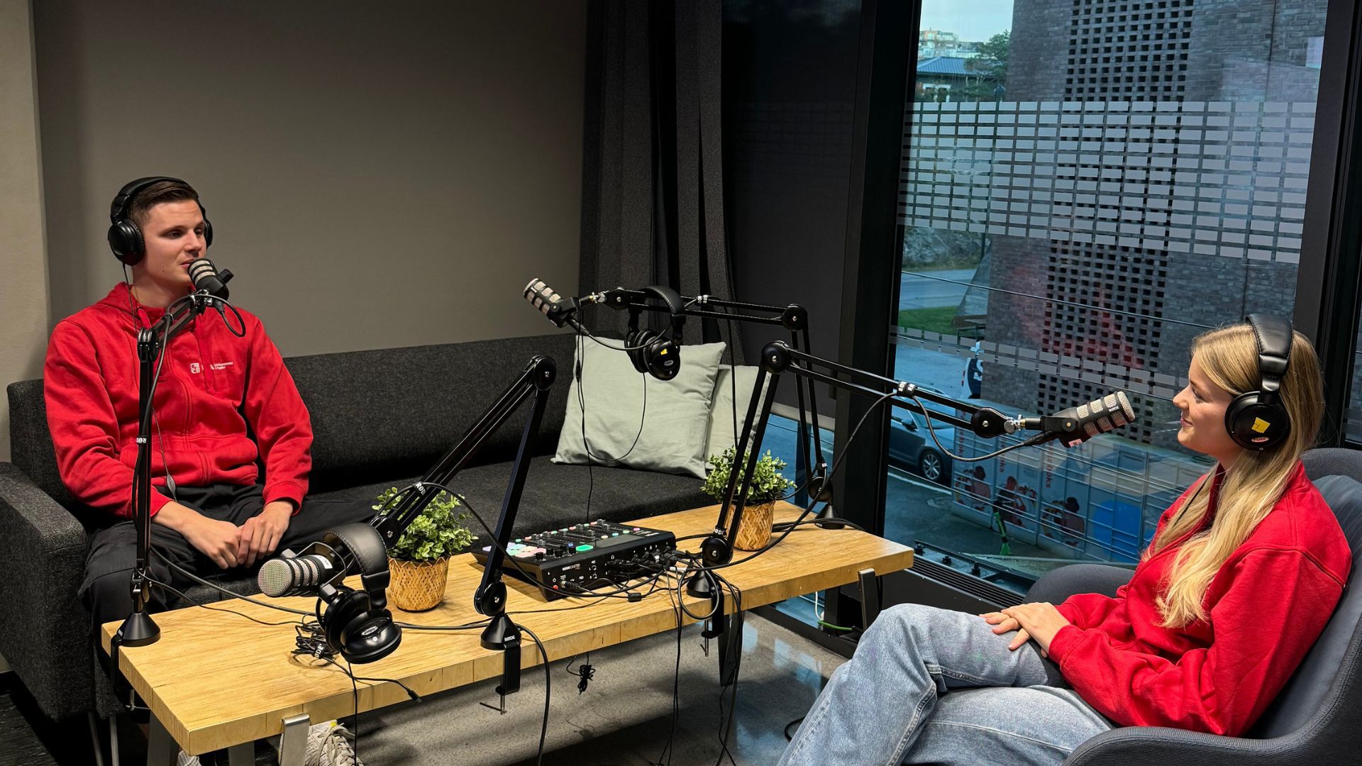 Bildet viser to studenter med røde UiA-gensere i et podkaststudio.