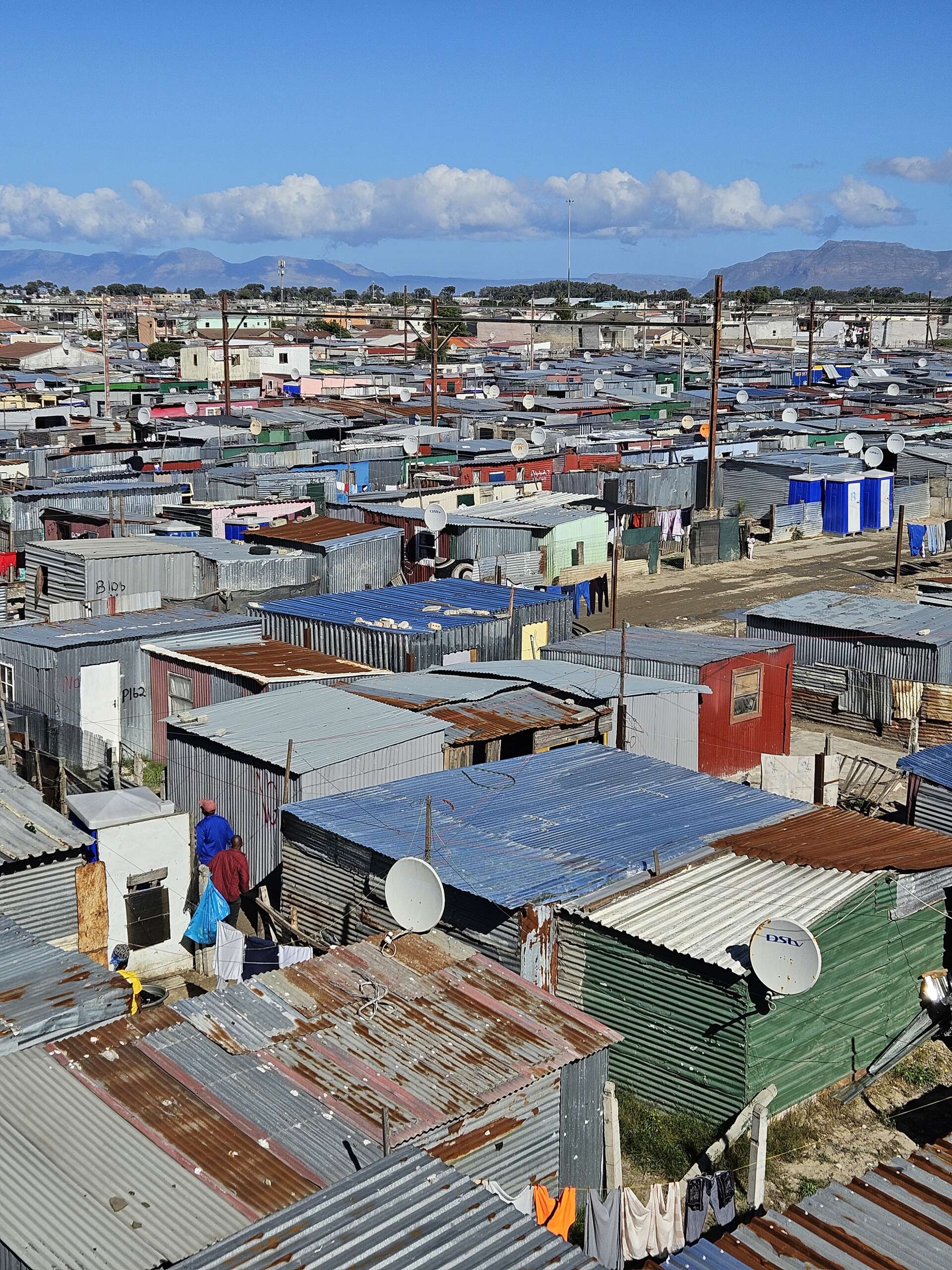 Tett bebyggelse med tak av bølgeblikk i Khayelitsha, med fjell i bakgrunnen.