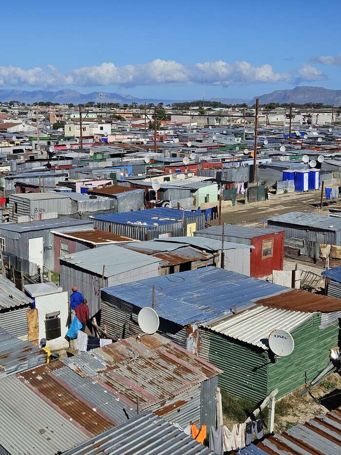 Tett bebyggelse med tak av bølgeblikk i Khayelitsha, med fjell i bakgrunnen.