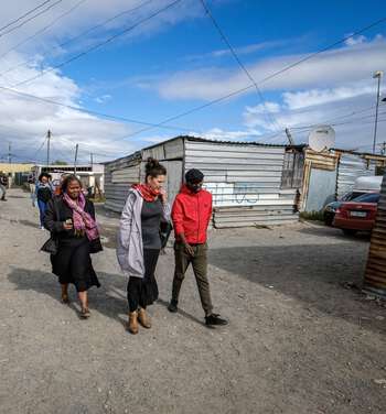 Tre personer går langs en gate med bygninger av bølgeblikk i Khayelitsha i Cape Town.