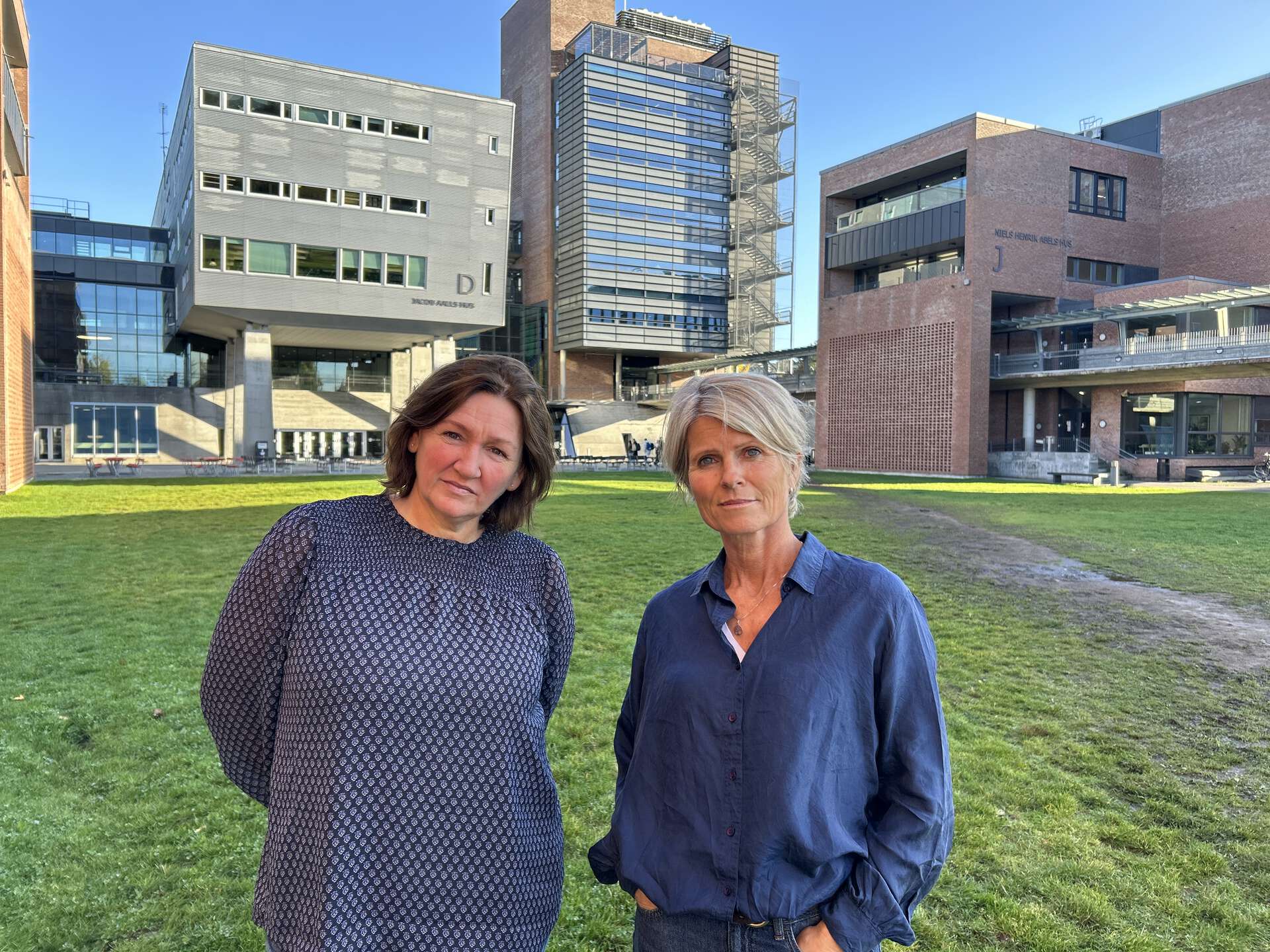 UiA-forskerne Hanne Haaland og Hege Wallevik står sammen utendørs foran universitetsbygninger.