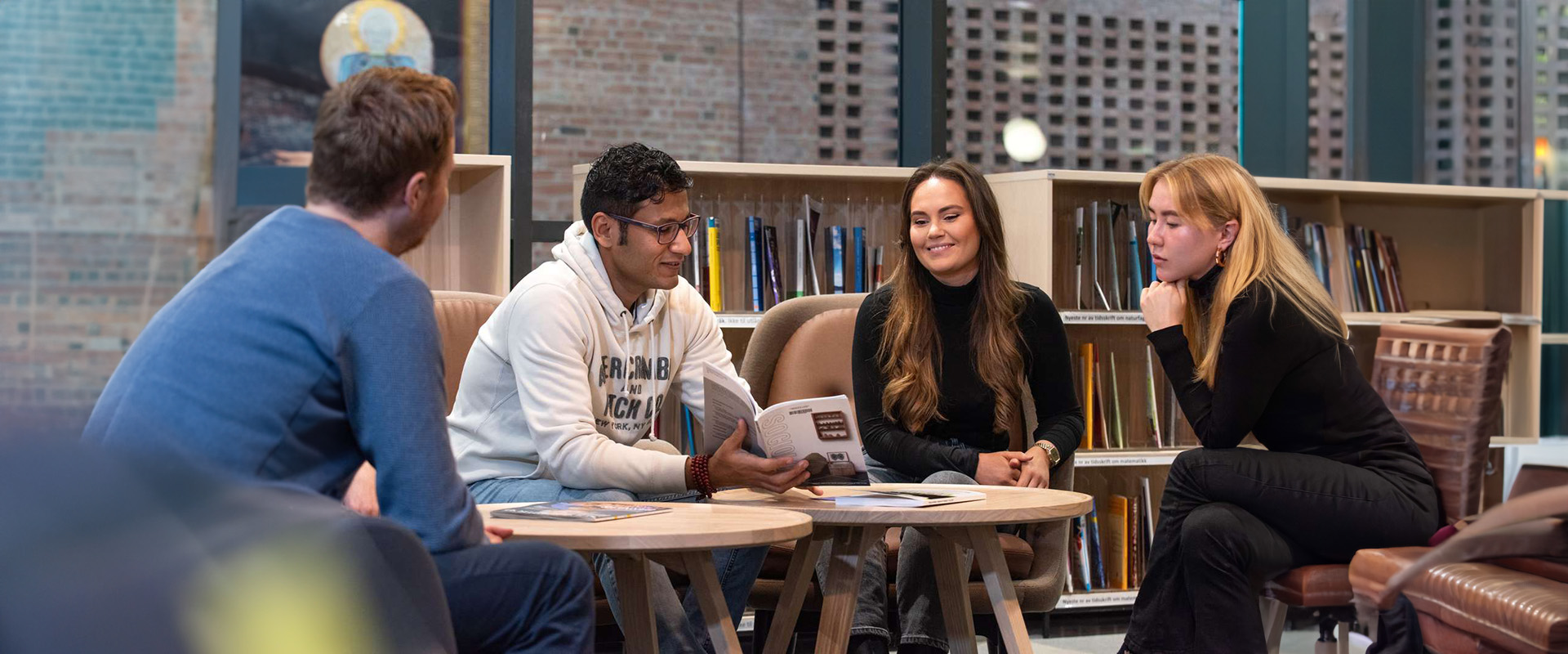 Fire studenter rundt et salongbord på biblioteket. Bøker og magasin på bordet