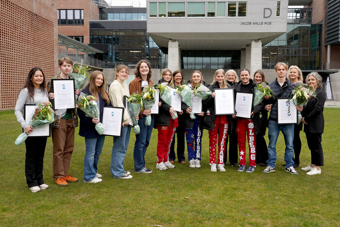 Prisvinnerne står på en gressplen foran universitetet med innrammet pris og blomster i hendene.