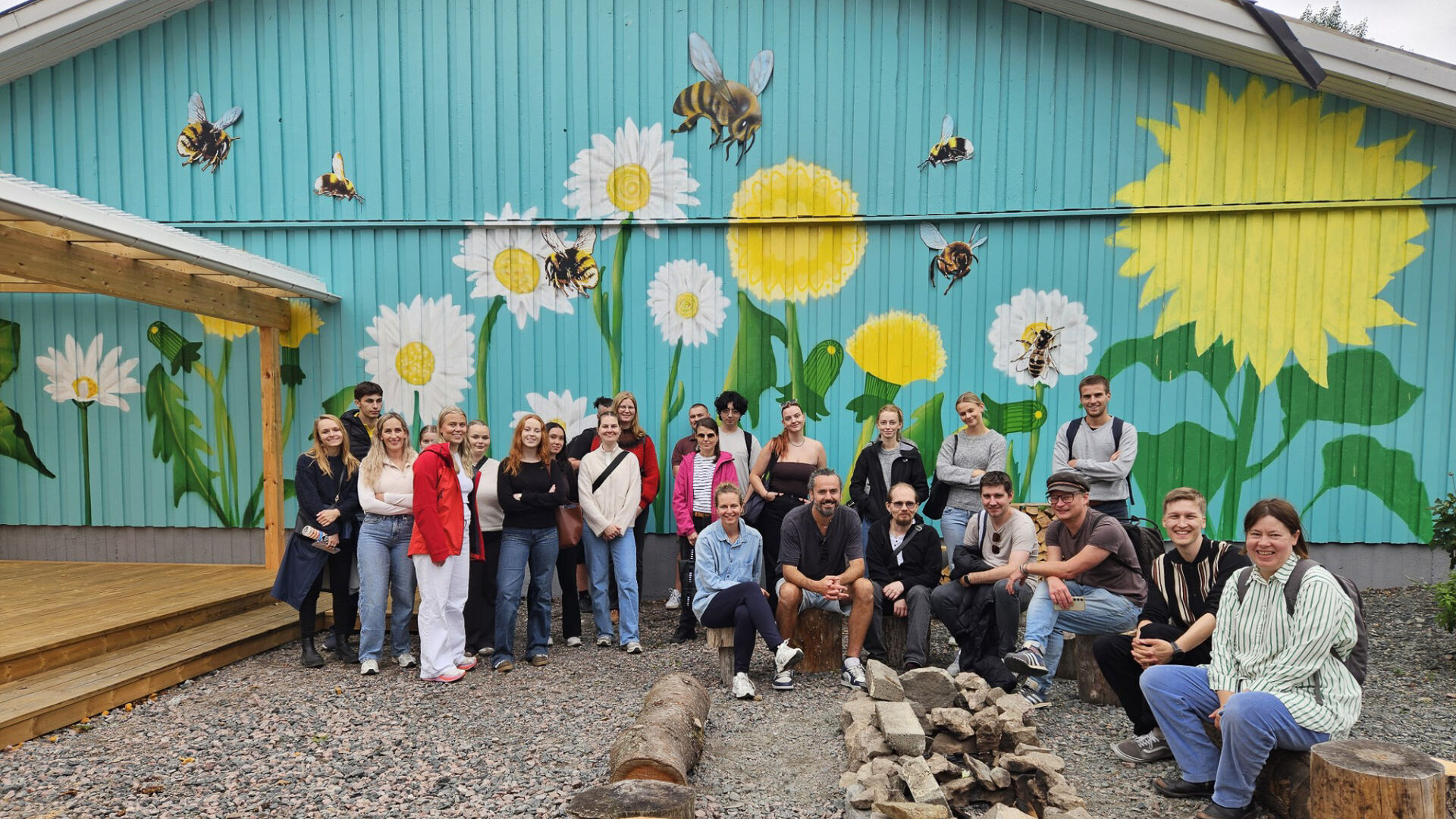 Gruppe med mennesker foran fargerik vegg med illustrasjoner av blomster og humler.