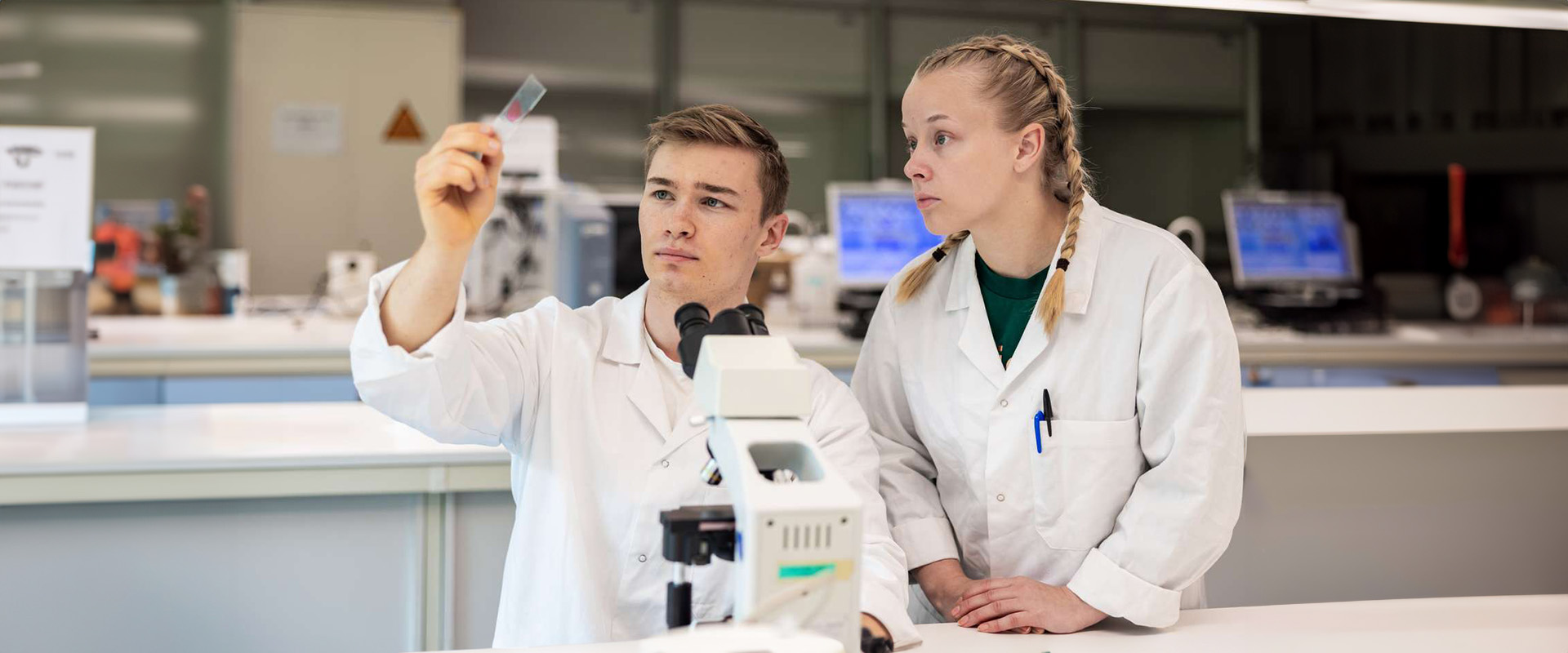 Two students at a laboratory, microscope, sample