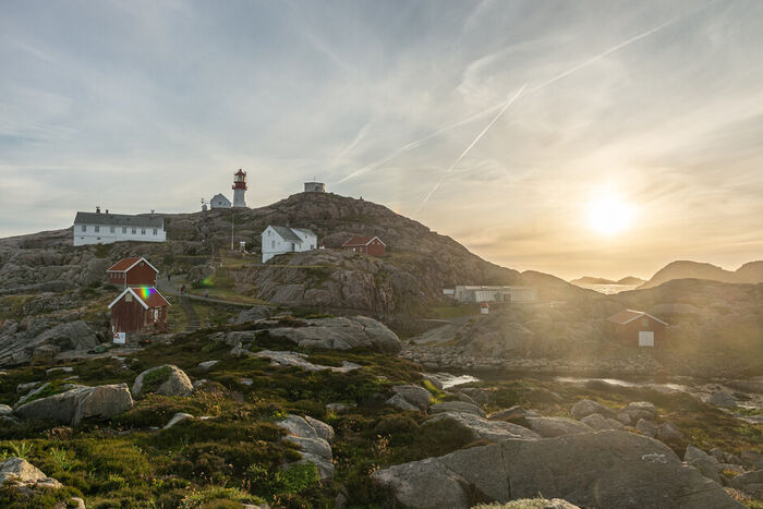 Bildet viser landskapet rundt Lindesnes fyr, med fyrtårnet i bakgrunden ved solnedgang