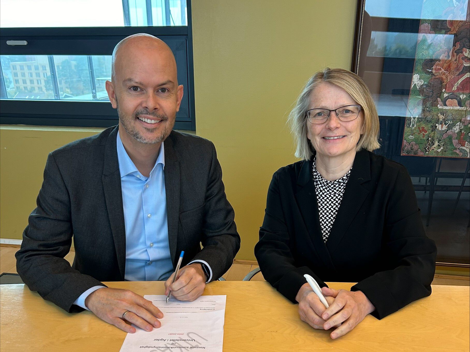 Bilde av to personer som signerer papir