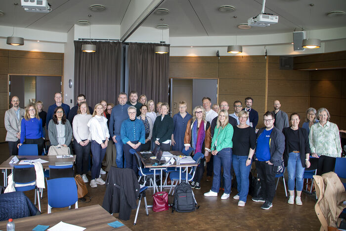 The photo shows around 30 people gathered in a conference room at a hotel.
