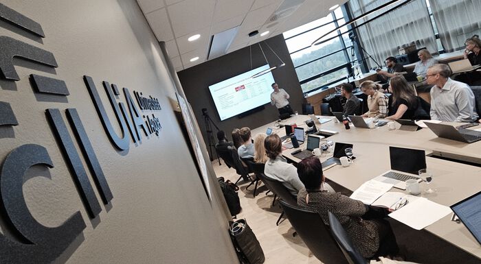 Board members seated around a table, university logo on the wall
