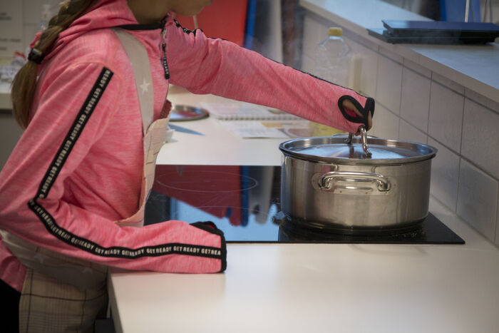 Elev med forkle som holder en gryte