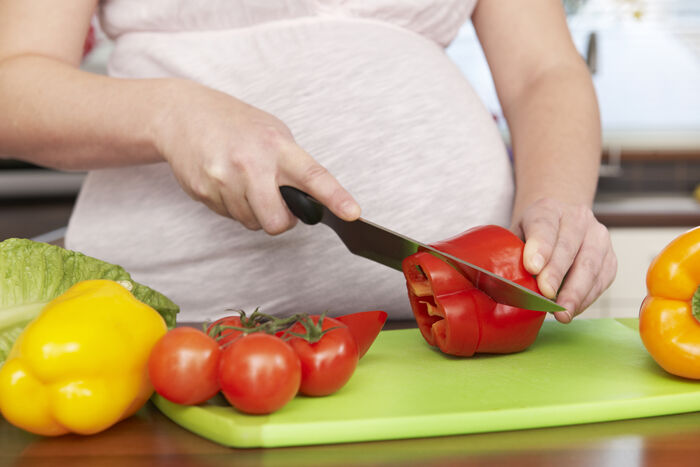 Gravid dame som kutter en rød paprika