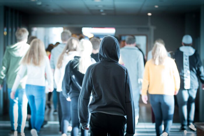 Gruppe elever i bakgrunnen går med ryggen til, en elev går alene bak