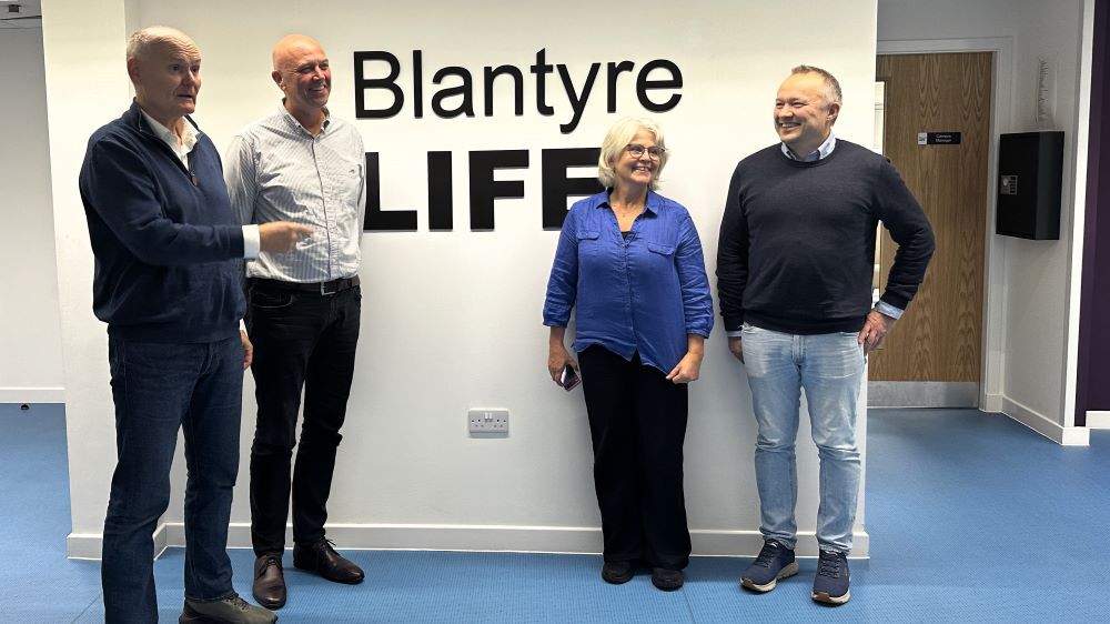 gruppebilde av 4 personer for en vegg det står blantyre life på