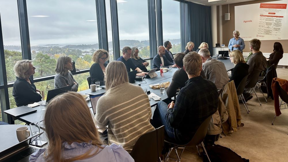 personer rundt et stort bord, person står og presenterer