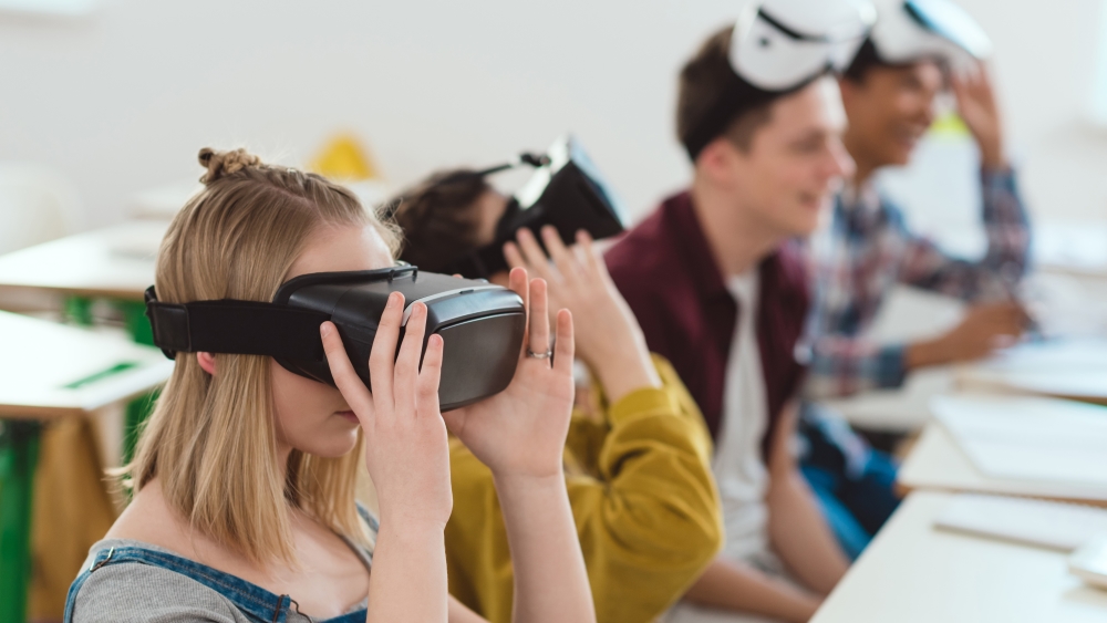 fire studenter sittande ved pulter med vr-briller på hovudet
