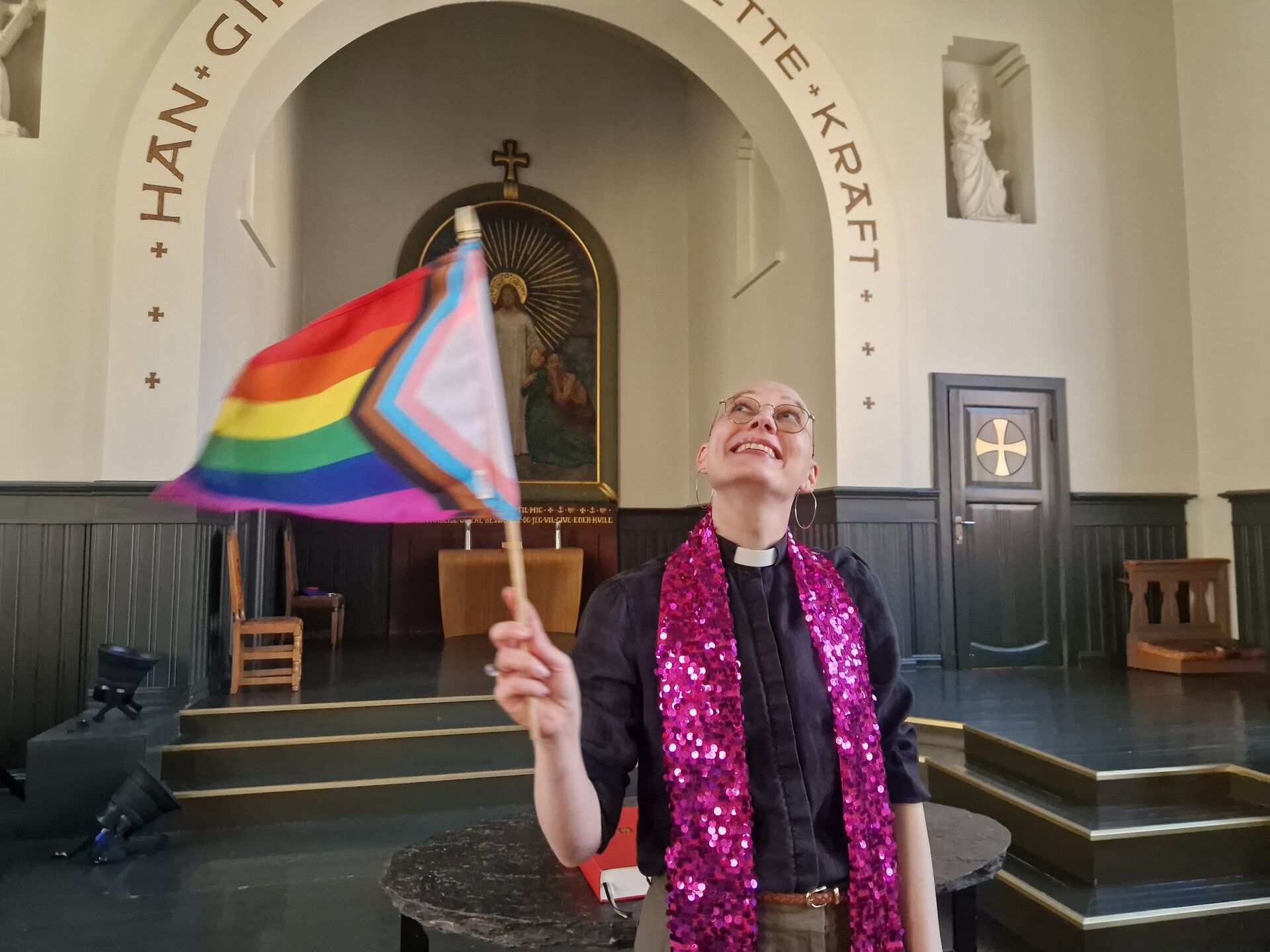 Prest som veiver med Pride-flagg i en kirke