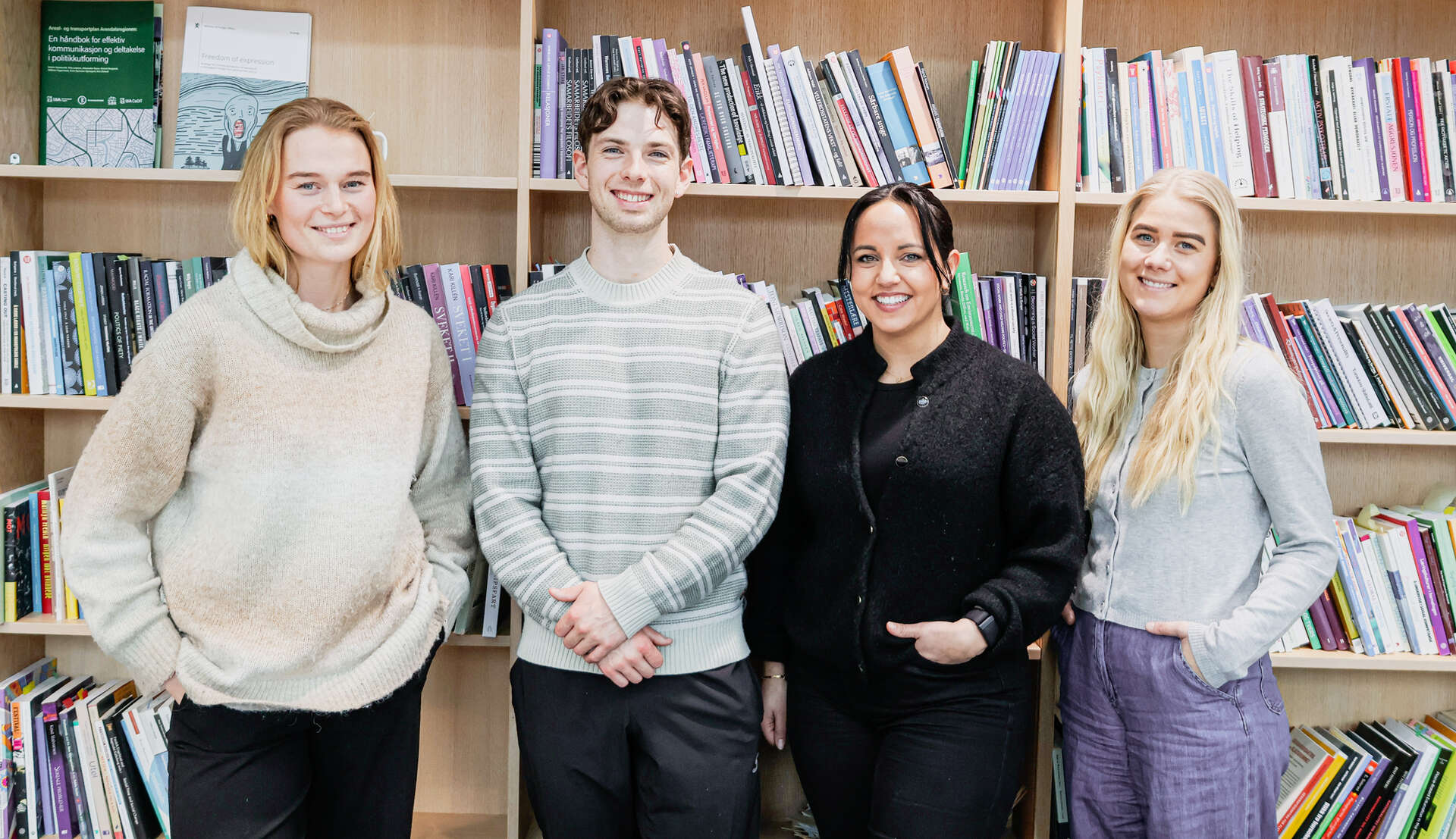Gruppebilde av fem smilende masterstudentene som står sammen bak flere bøker