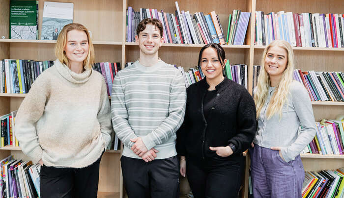 Gruppebilde av fem smilende masterstudentene som står sammen bak flere bøker