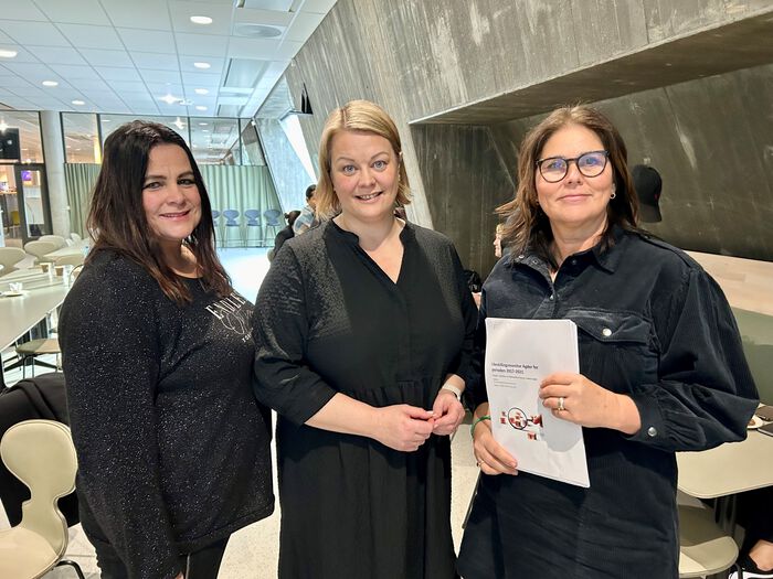 Fra venstre seniorforsker Nina Jentoft fra NORCE, konserndirektør Eva Kvelland fra Sparebanken Sør og seniorrådgiver Åsta Lovise Einstabland fra Senter for likestilling da første del av årets likestillingsmonitor ble lagt frem i Lilletun-stova på Universitetet i Agder i Kristiansand. De står ved siden av hverandre og smiler mot kamera. Einstabland holder en bunke papirer i hånda. 