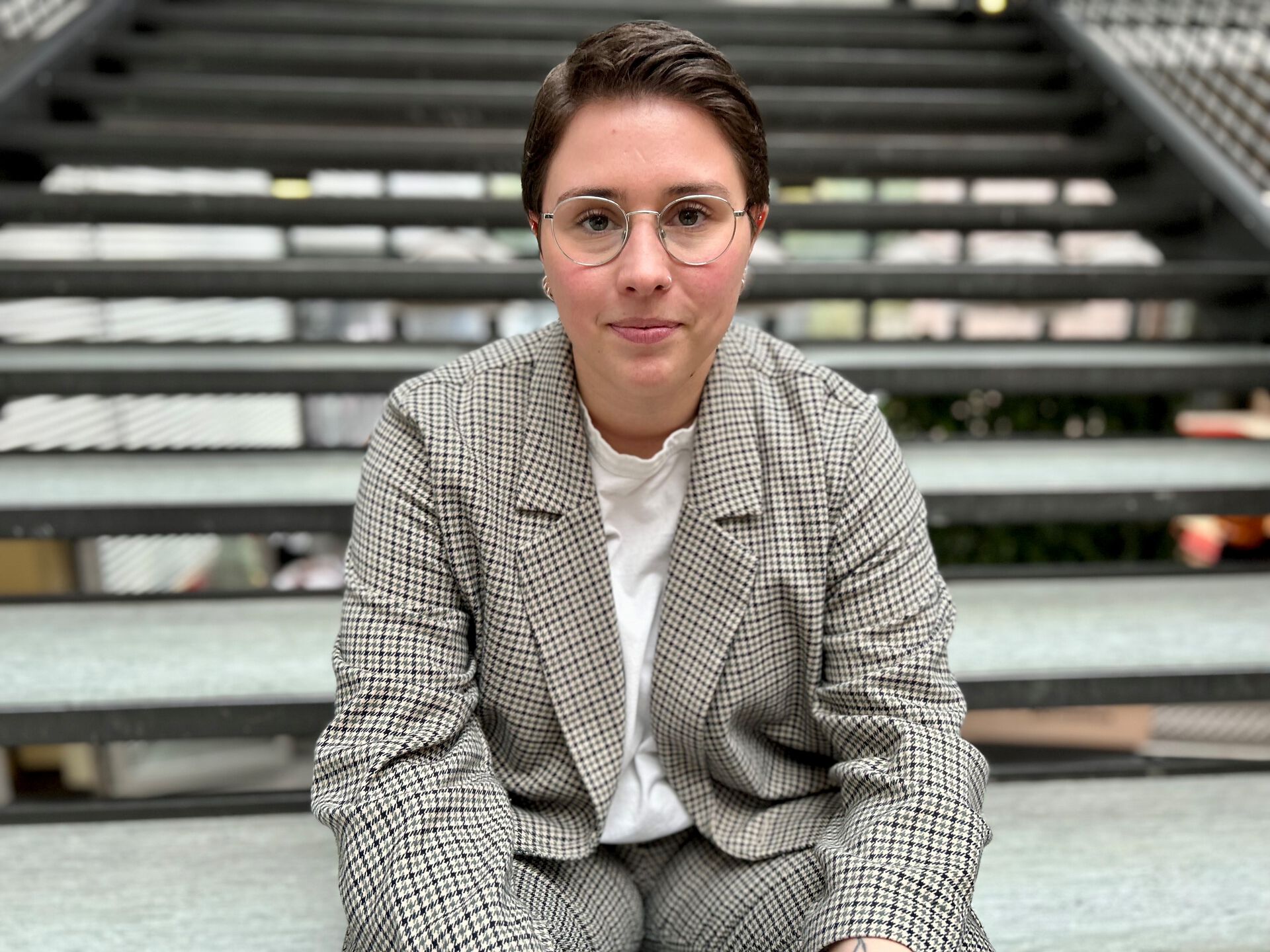 Thea Litschi sitter i trappa ved Vrimlehallen på UiA. Hun ser mot kamera og smiler litt. 