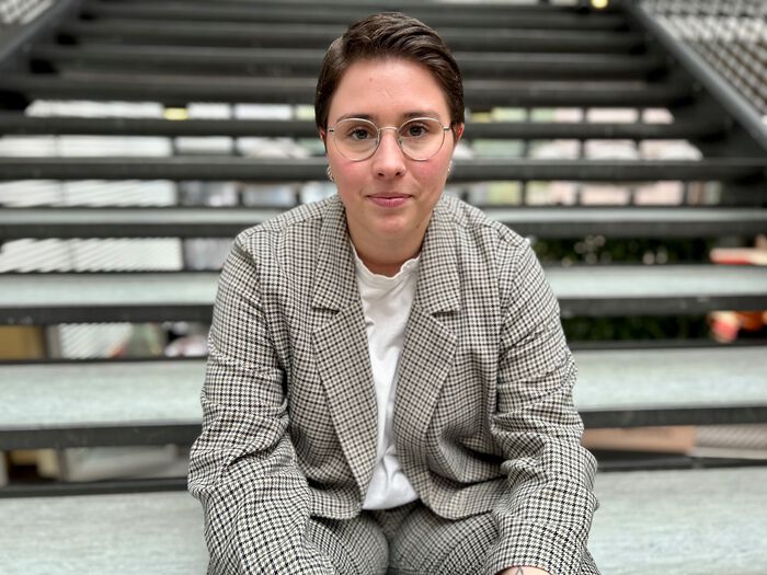 Thea Litschi sitter i trappa ved Vrimlehallen på UiA. Hun ser mot kamera og smiler litt. 