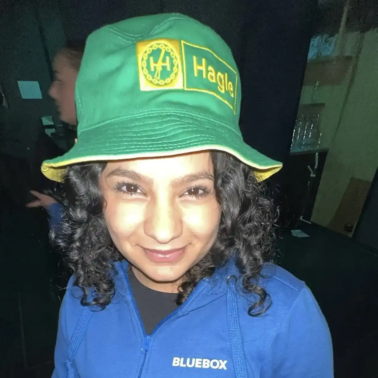 Rolian avbildet med blå Bluebox-jakke og grønn og gul bøttehatt med teksten "Hagle" i Felleskjøpet-stil. Bilde tatt i forbindelse med en konsert med Hagle på Bluebox.