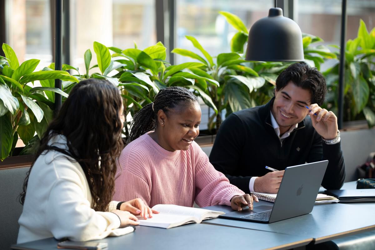 Bilde av tre studenter som sitter og snakker sammen og ser på en PC
