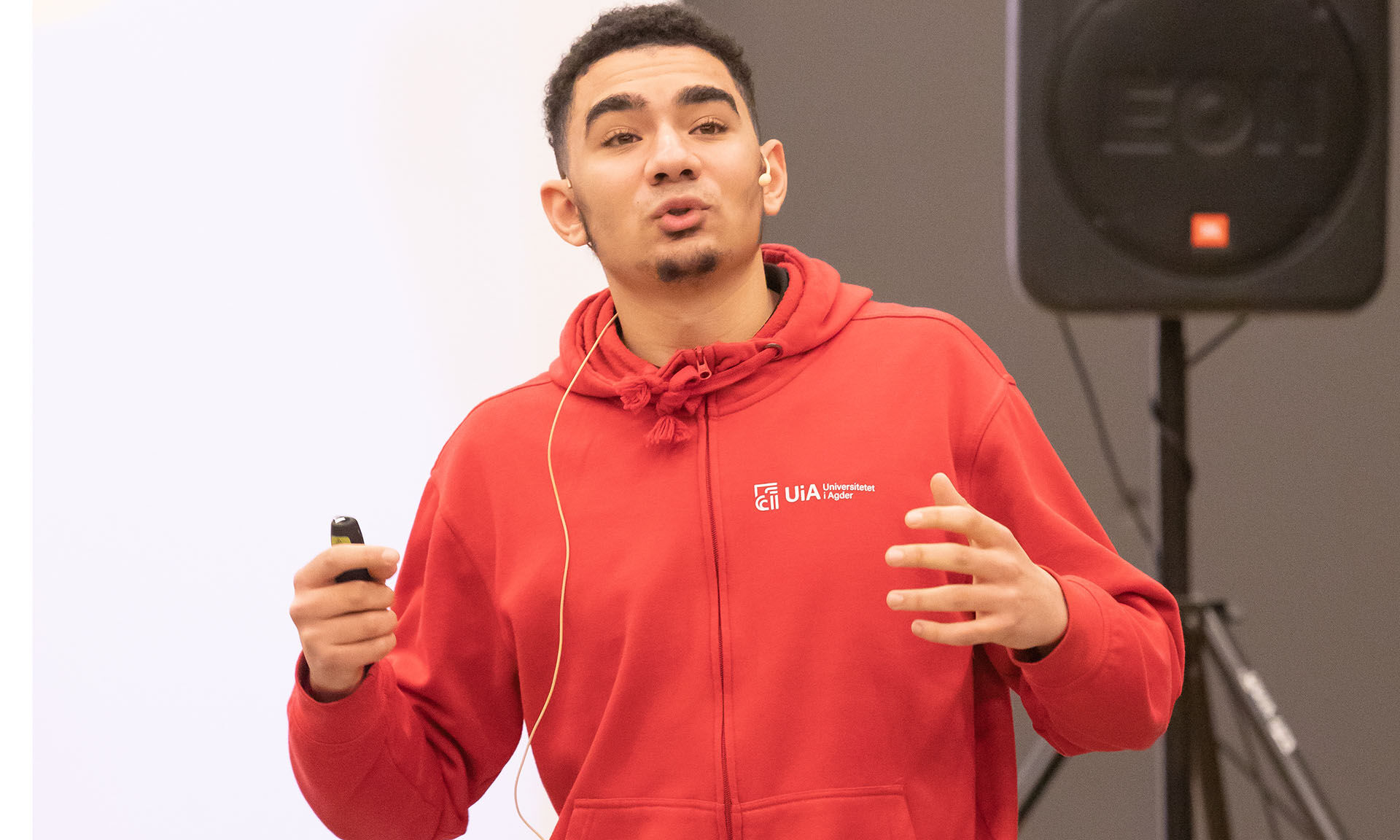 Studentambassadør Adam holder presentasjon om UiA på skolebesøksturneen. Ikledd rødt UiA-tøy, og med klikker i hånda.