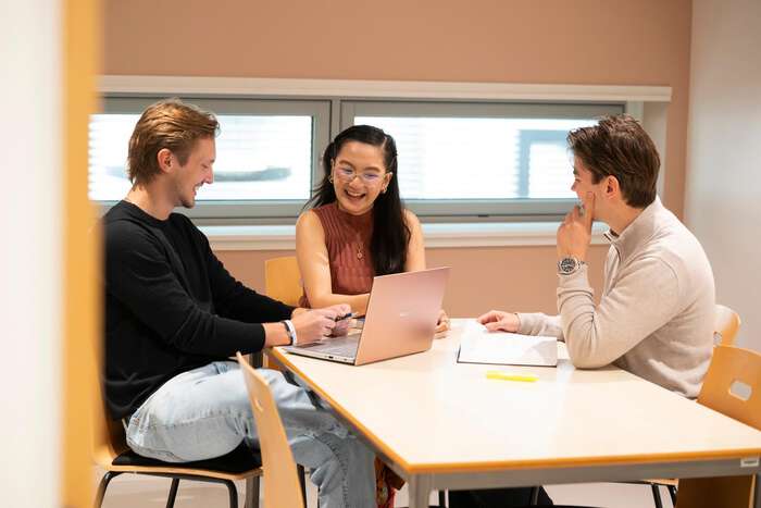 Tre studenter snakker sammen ved en laptop på et grupperom