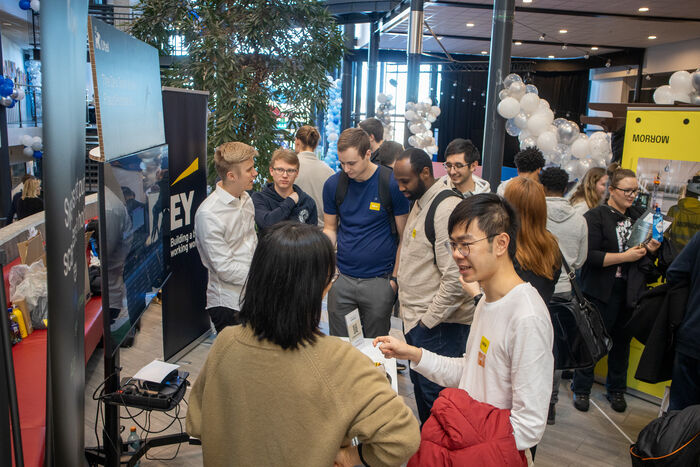Engasjerte studenter snakker med noen på stand fra EY. 